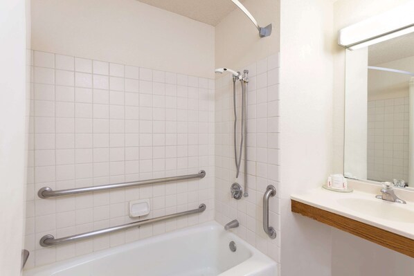 Un baño con bañera, barras de apoyo, cabezal de ducha y espejo.