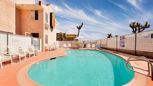 A swimming pool surrounded by lounge chairs and a fenced area with a building in the background. - Super 8 by Wyndham Yucca Val/Joshua Tree Nat Pk Area (Yucca Valley)