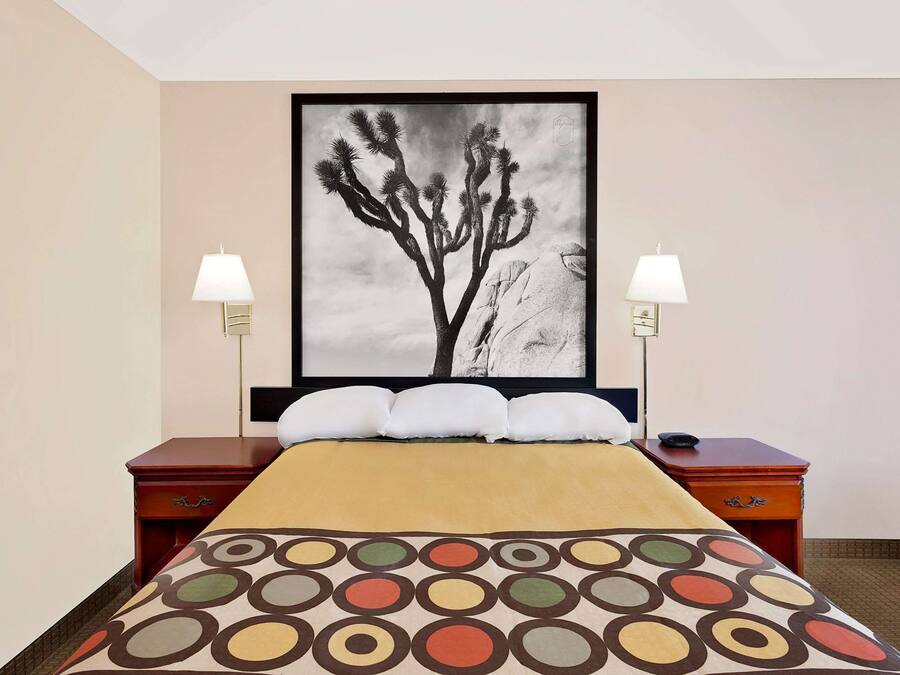 A hotel room with a bed, two bedside tables, a large framed artwork on the wall, and two wall-mounted lamps.