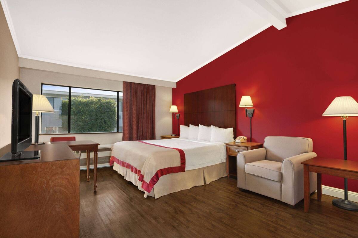 A hotel room with a large bed, a desk, a chair, and a TV.