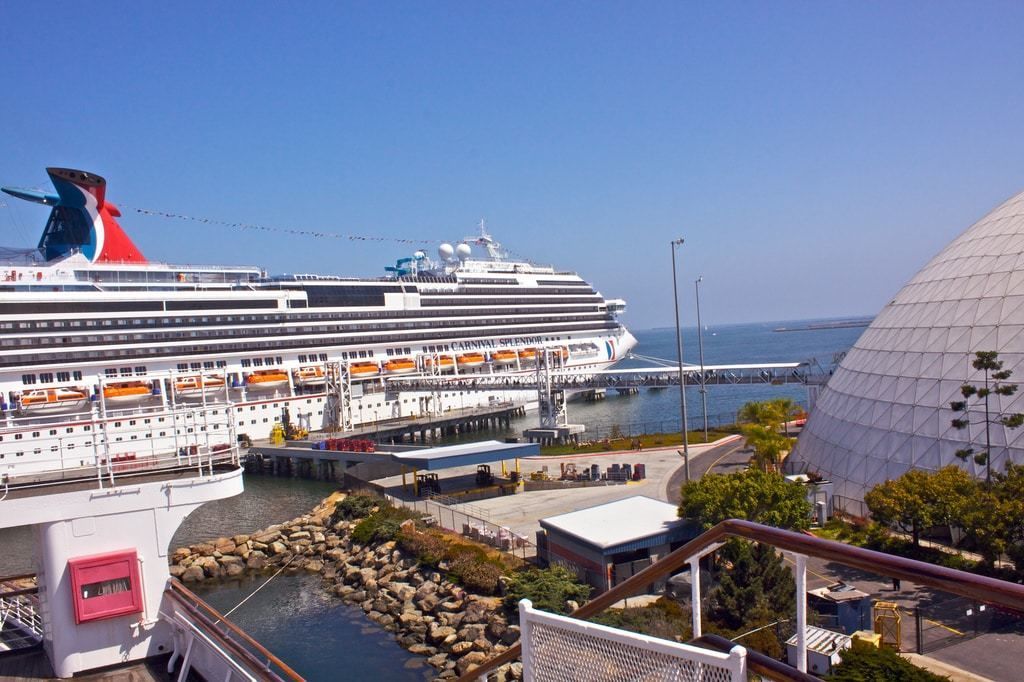 A large cruise ship docked at a port with a modern dome structure nearby.