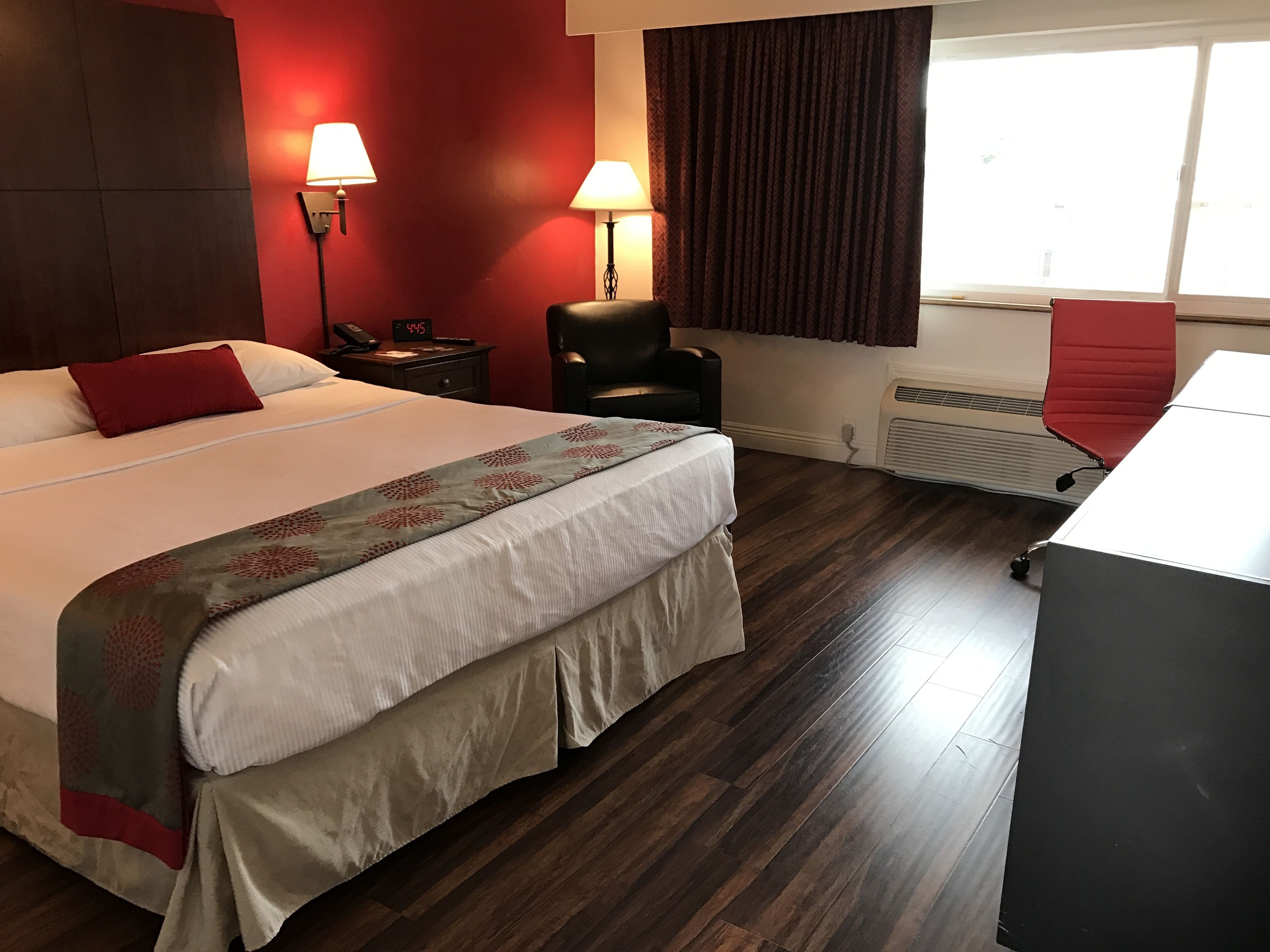 Una habitación de hotel con una cama grande, dos lámparas de noche, una silla, un escritorio y una ventana con cortinas.