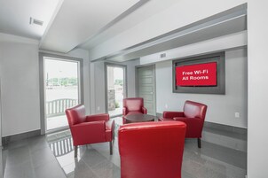 Quarto de hotel com sofá vermelho, mesa pequena e placa indicando Wi-Fi gratuito em todas as acomodações.