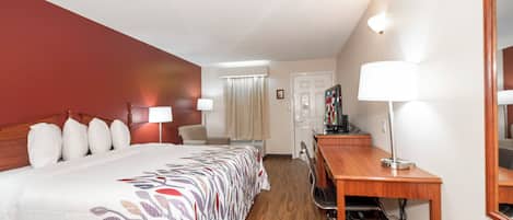 A hotel room with a bed, desk, chair, and a television.