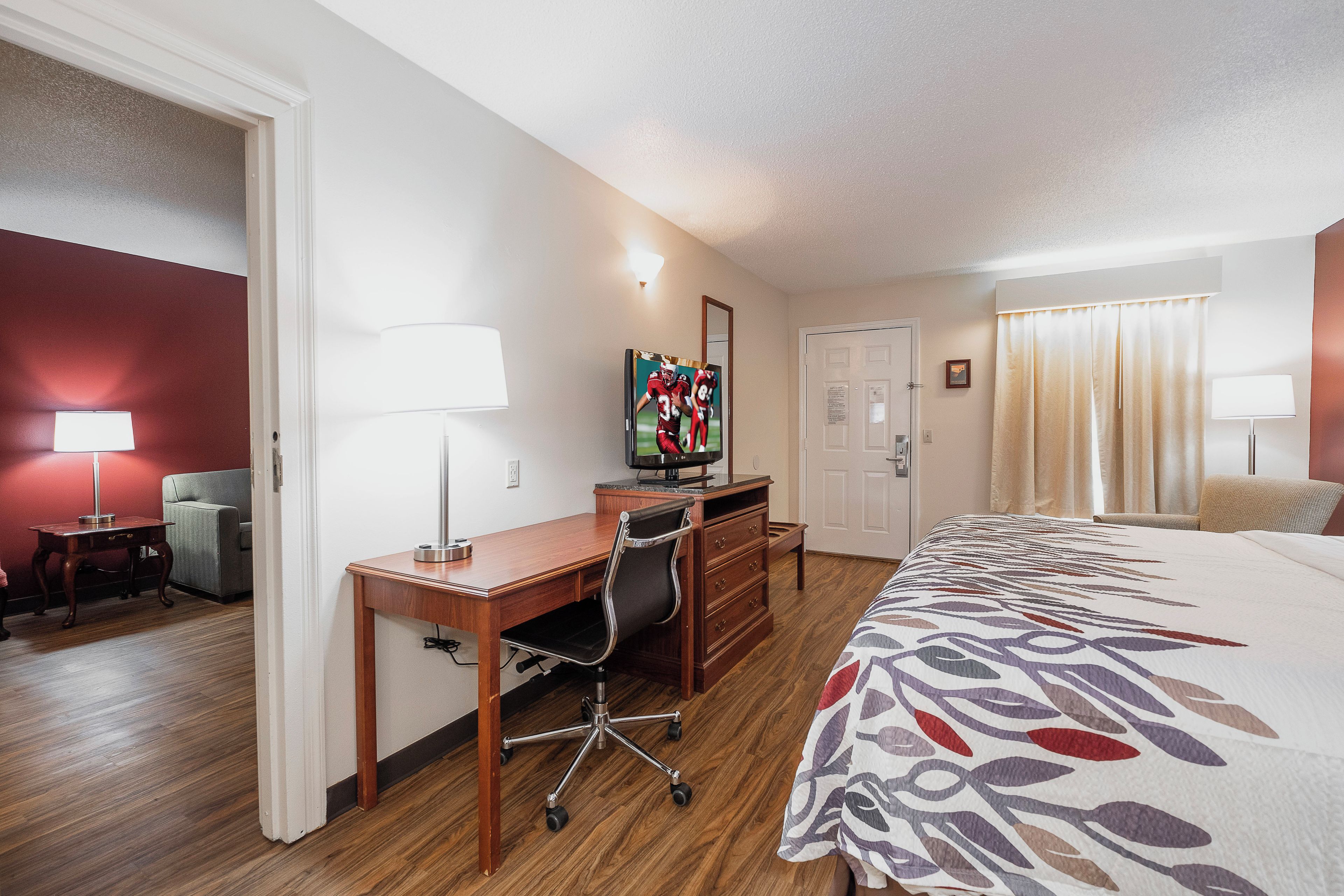 A hotel room with a bed, desk, chair, television, and a door.