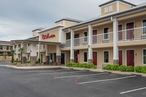 A hotel with a red and white sign, multiple balconies, and a parking lot.