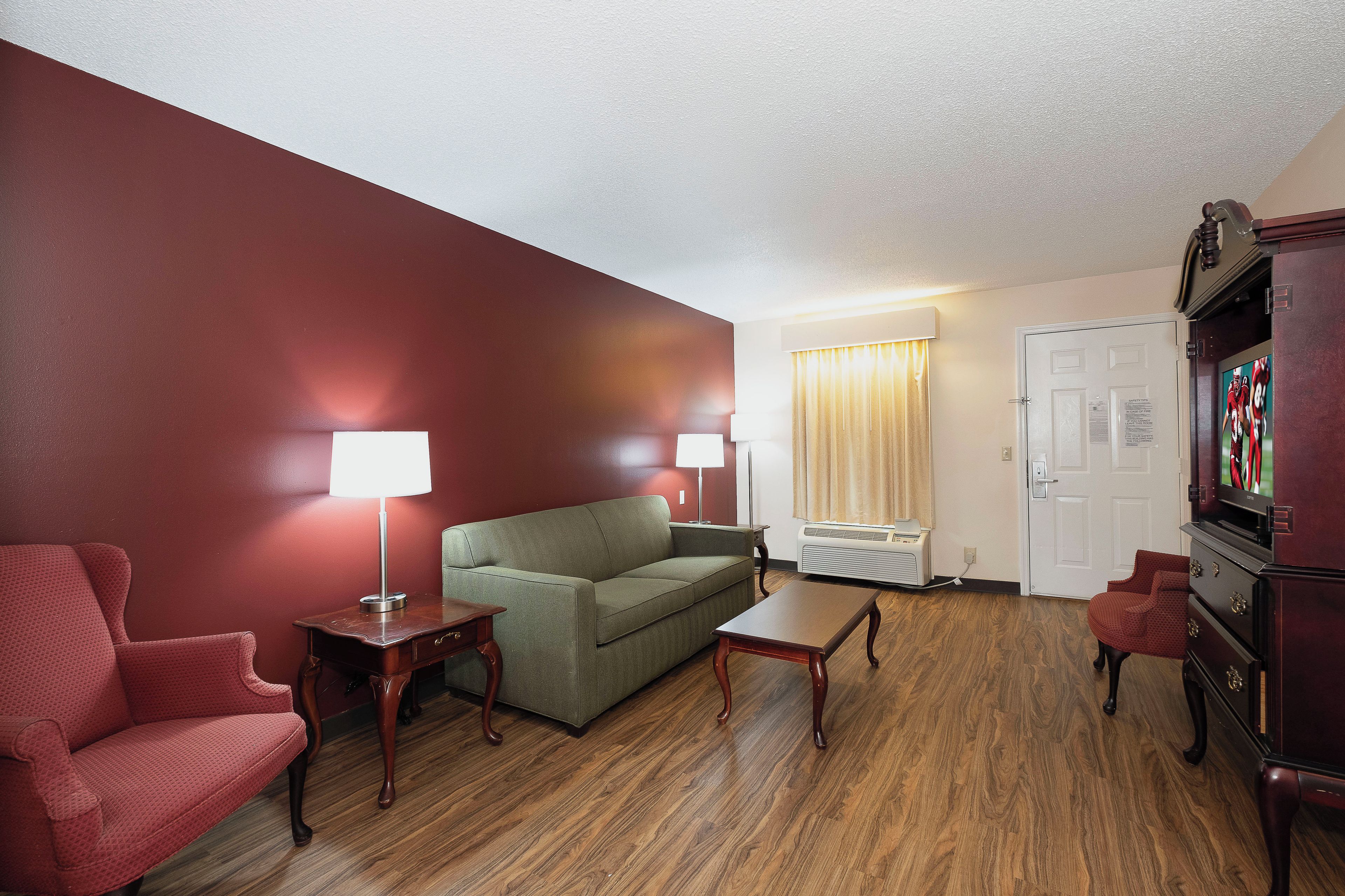 Una sala de estar con un sofá verde, un sillón rojo, una mesa de centro de madera y un televisor sobre un mueble.
