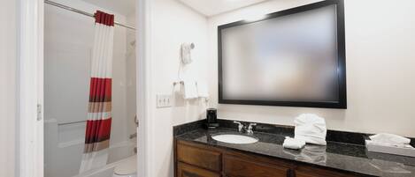 A bathroom with a shower curtain, a toilet, a sink with a mirror above it, and a towel on the counter.