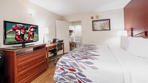 A hotel room with a bed, a desk, a television, a chair, and a bathroom visible through an open door.