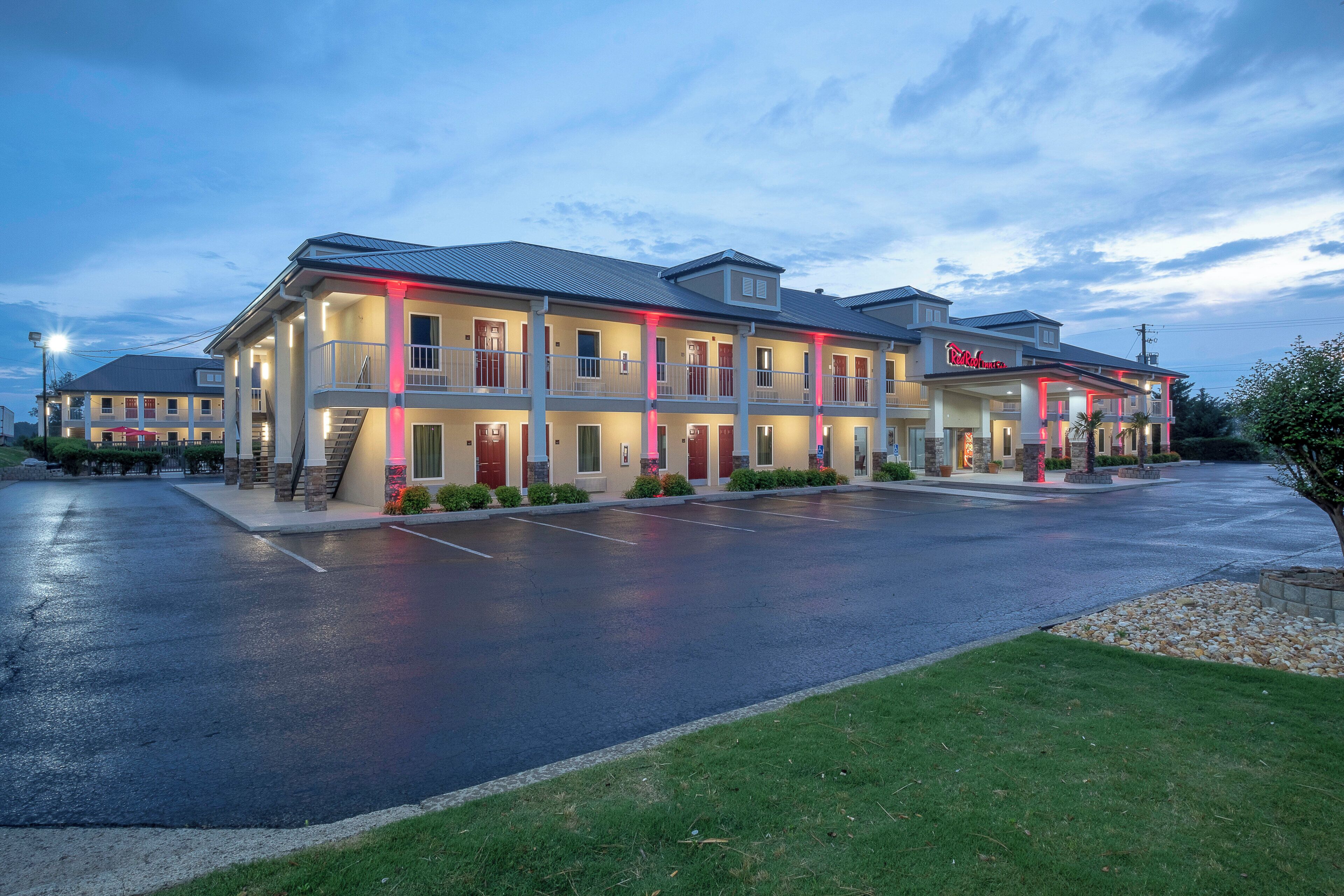 A multi-story hotel with a flat roof, a covered front porch, and a parking lot.