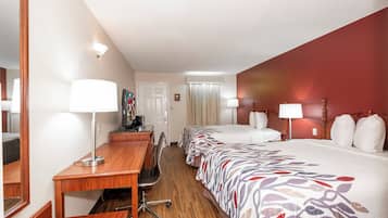 Une chambre d’hôtel avec un bureau en bois, deux lits avec une literie à motifs, une télévision et un miroir.