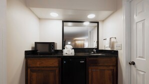 A bathroom with a black countertop, a microwave, a sink, and a mirror.