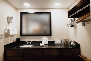 A hotel bathroom with a large mirror, a sink, a towel rack, and a coffee maker.