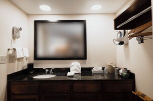 Un baño de hotel con un espejo grande, un lavamanos, un perchero para toallas y una cafetera.