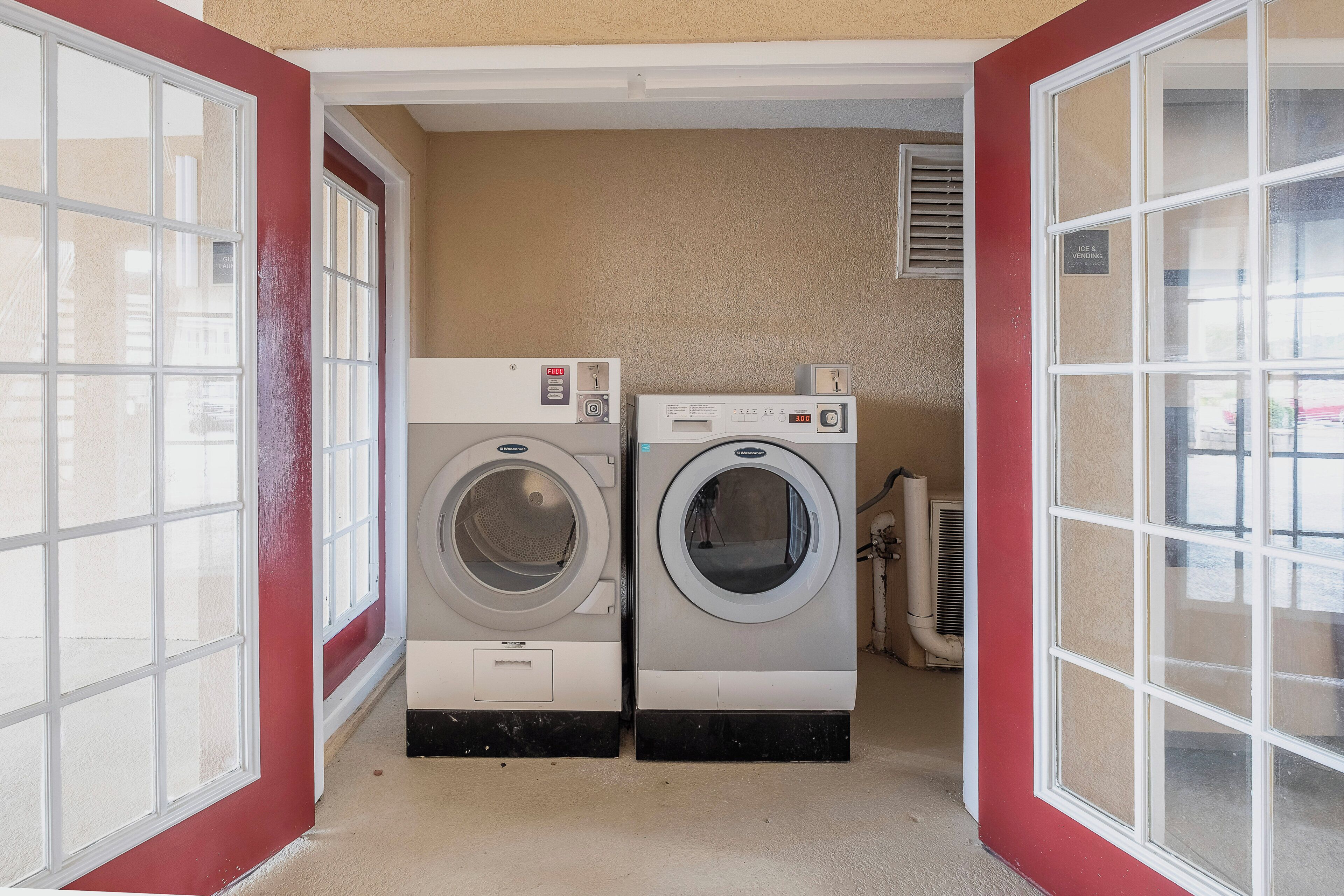 A laundry room with two front-loading washers and dryers, a vent, and a sign indicating ice and vending services.