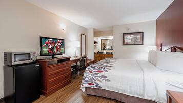 A hotel room with a bed, a desk, a television, a dresser, a mirror, and a picture on the wall.