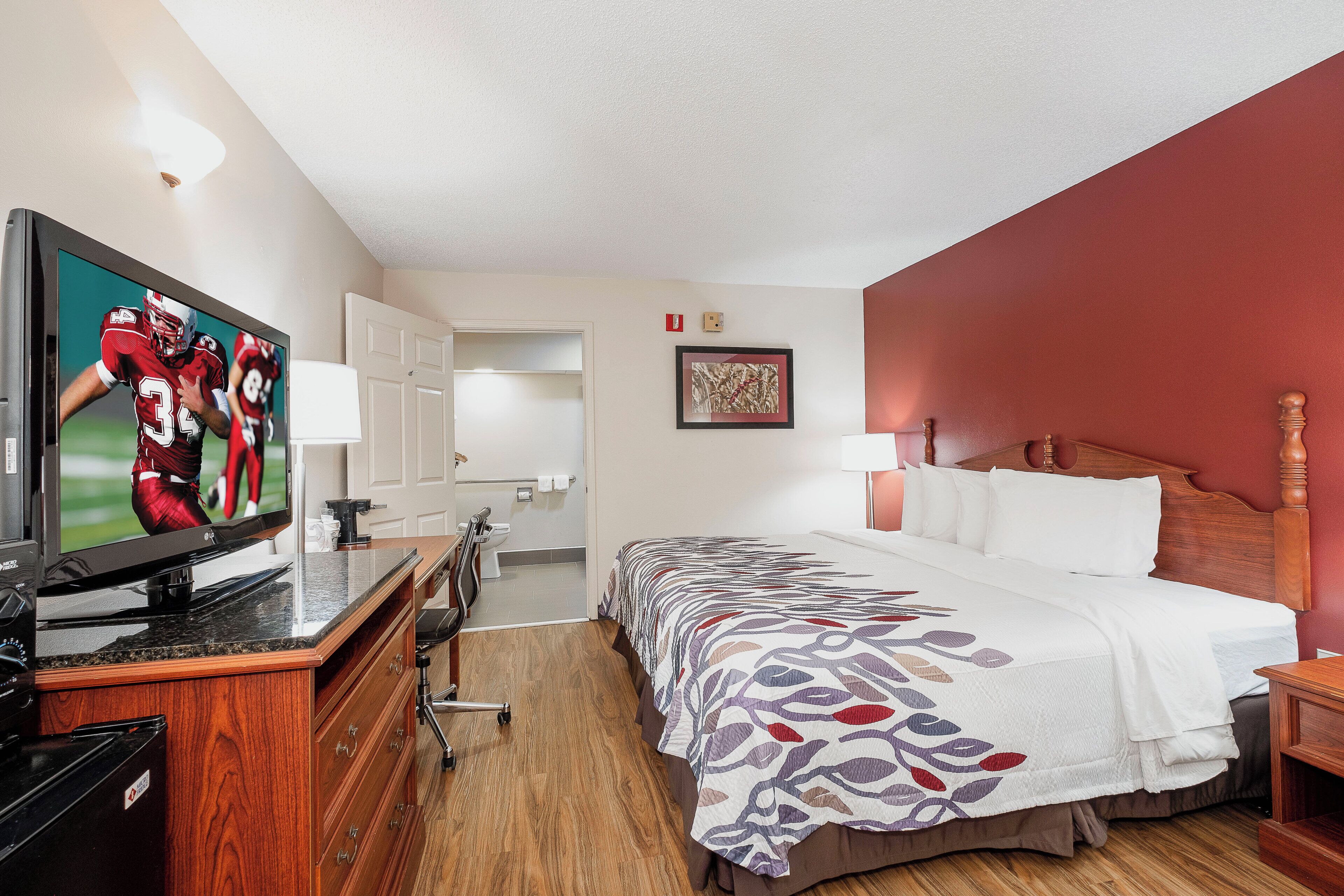 A hotel room with a bed, a television, a desk, and a bathroom.