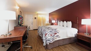A hotel room with a bed, desk, chair, and lamps.