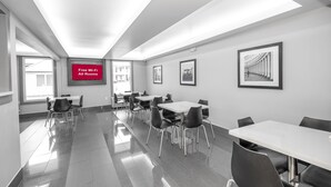 A modern conference room with white tables and chairs, a large screen displaying "Free Wi-Fi All Rooms," and framed pictures on the walls.