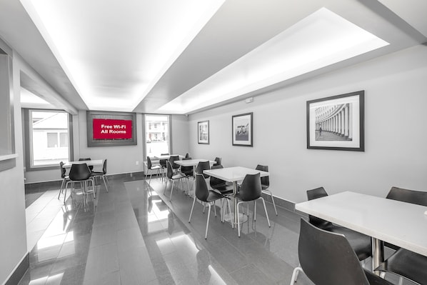 A modern conference room with white tables and chairs, a large screen displaying "Free Wi-Fi All Rooms," and framed pictures on the walls.