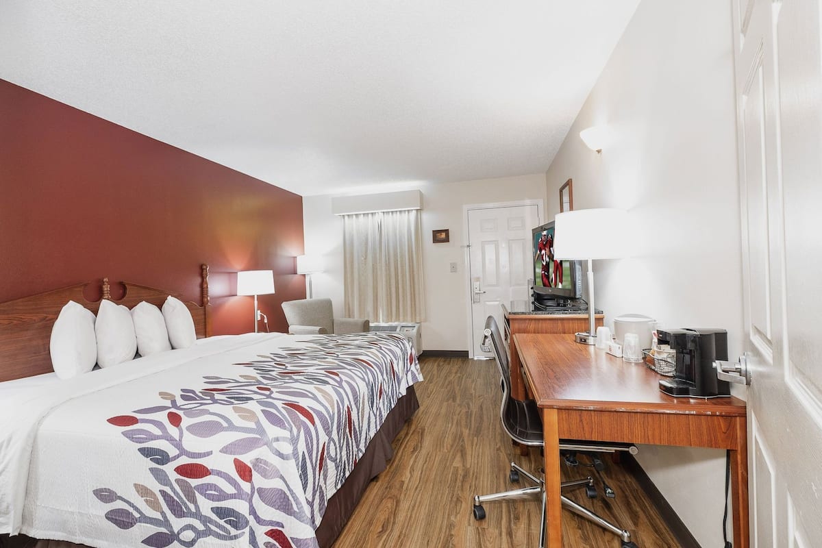 Ein Hotelzimmer mit Bett, Schreibtisch, Stuhl, Fernseher und Kaffeemaschine.