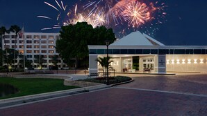 A hotel entrance with a landscaped area, a fountain, and a view of fireworks in the background. - Holiday Inn Resort Kissimmee by the Parks by IHG (Kissimmee)