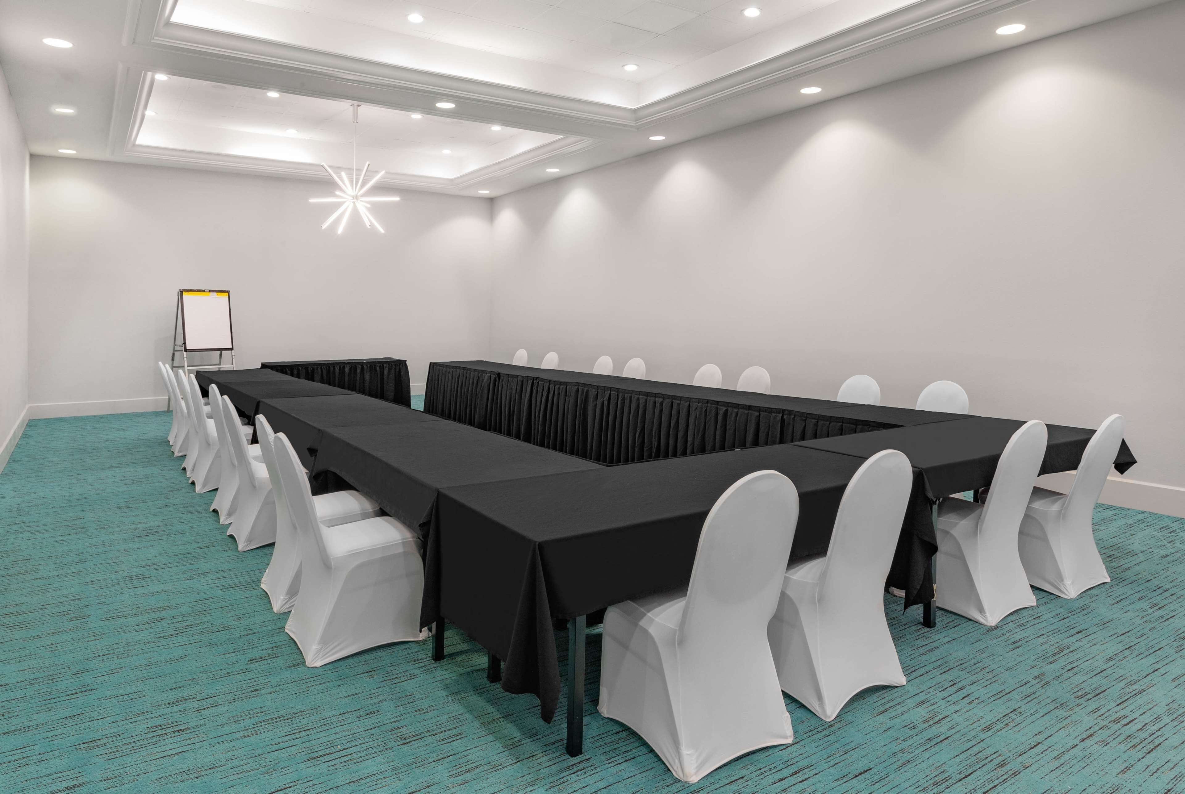 Un salón de conferencias con una larga mesa, sillas blancas y una pizarra.