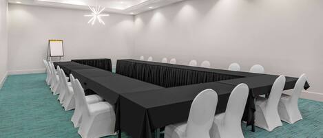 Un salón de conferencias con una larga mesa, sillas blancas y una pizarra.