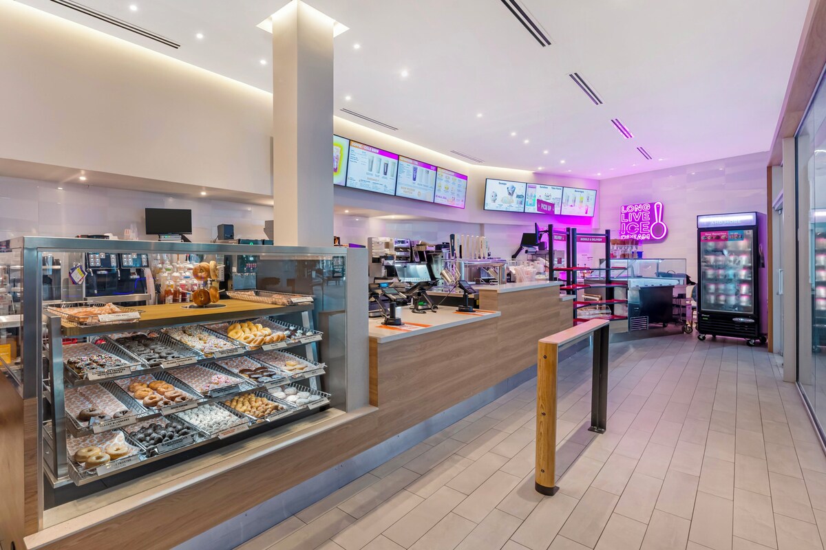 A modern bakery counter with a variety of baked goods, a digital menu display, and a neon sign. - Holiday Inn Resort Kissimmee by the Parks by IHG (Kissimmee)