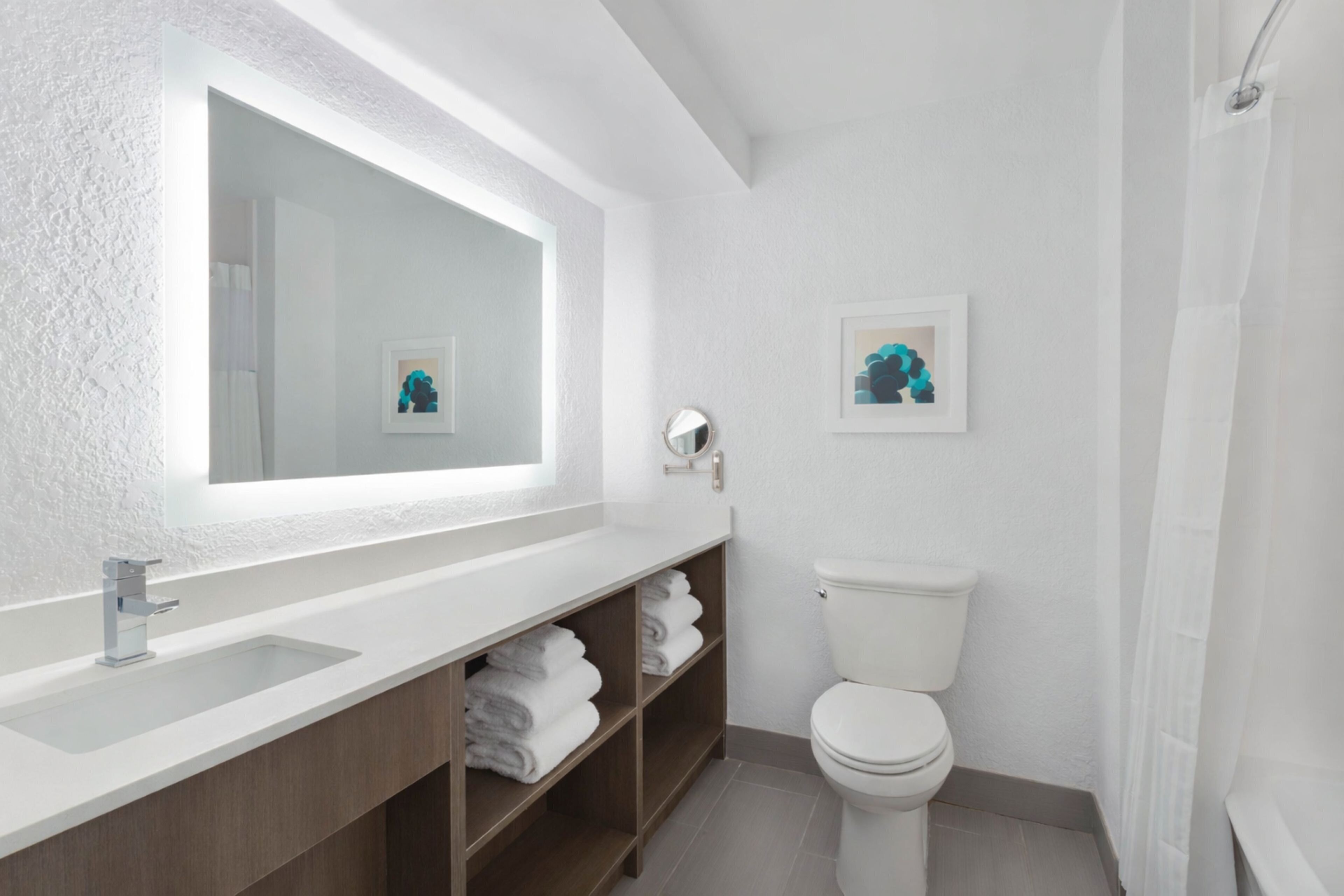 Ein modernes Badezimmer mit einem großen Spiegel, einem weißen Waschbecken, einer Toilette und einer Duschkabine.