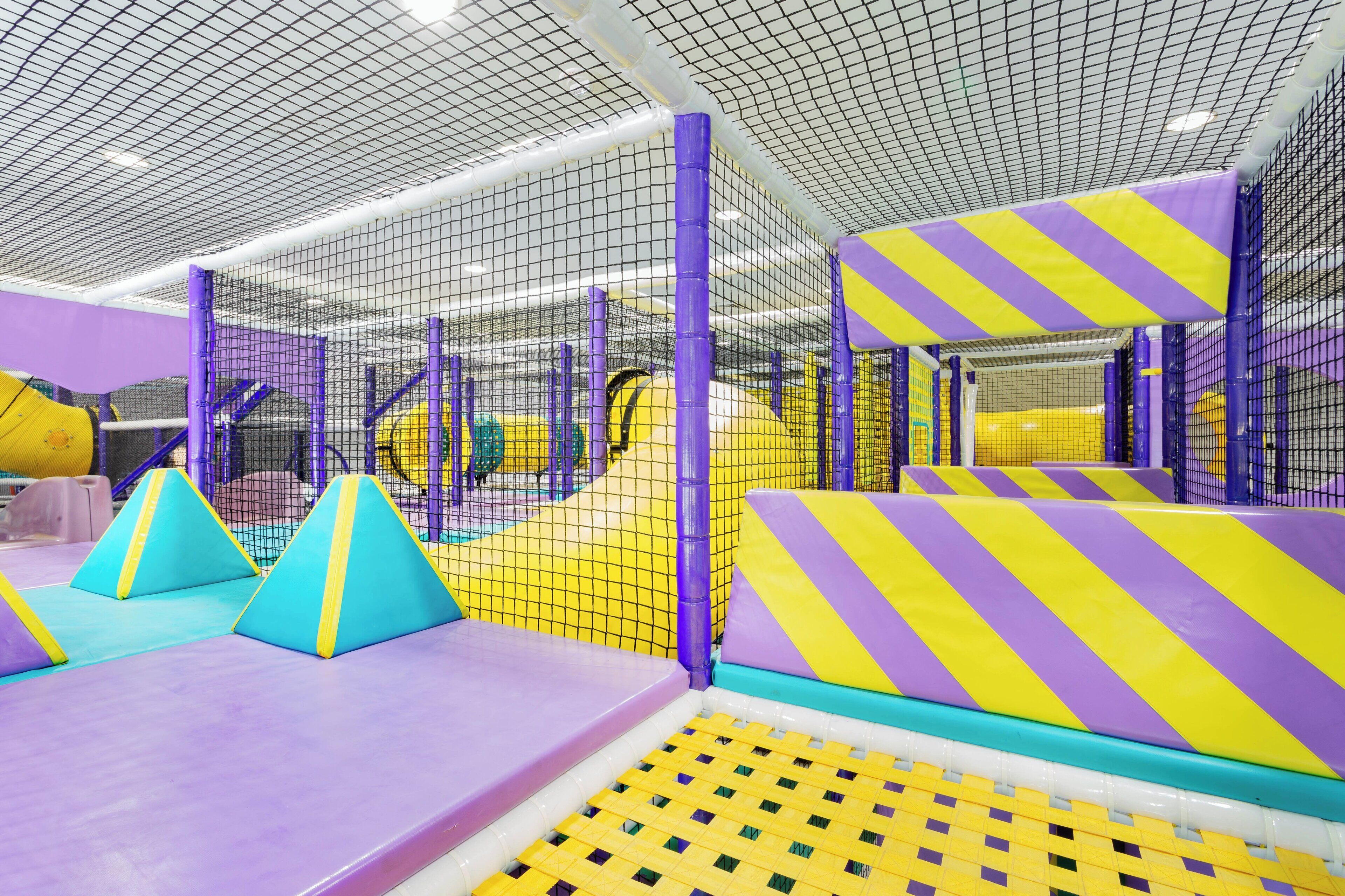 An indoor play area with padded climbing structures and netted walls.