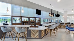 A modern bar area with high stools, a long counter, and a large window offering a view of the outdoors. - Holiday Inn Resort Kissimmee by the Parks by IHG (Kissimmee)