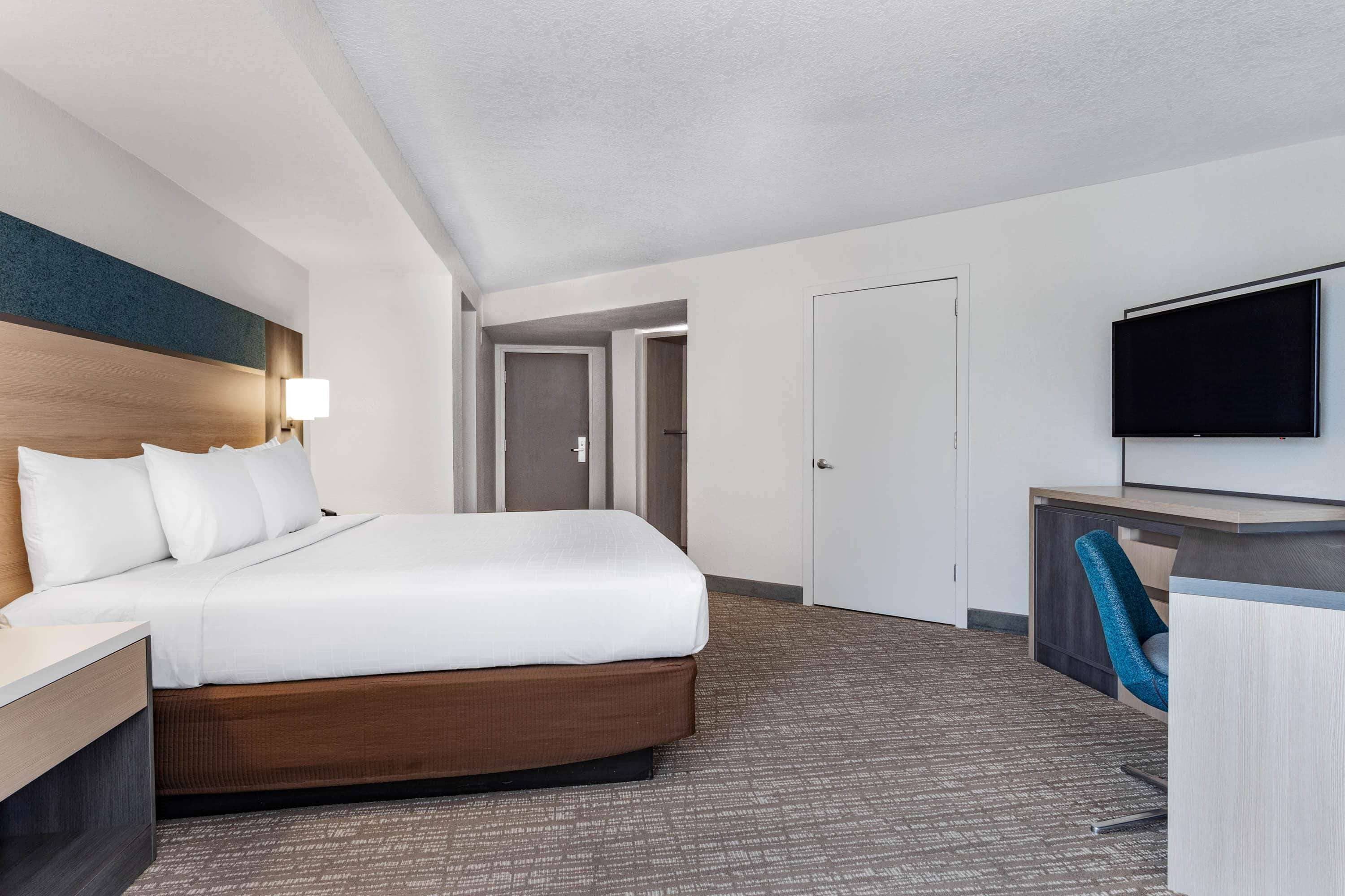 Une chambre d’hôtel avec un grand lit, un bureau avec une chaise, un téléviseur à écran plat et une porte donnant sur une autre pièce.