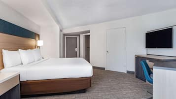 Une chambre d’hôtel avec un grand lit, un bureau avec une chaise, un téléviseur à écran plat et une porte donnant sur une autre pièce.