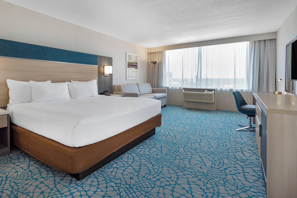 Een hotelkamer met een groot bed, een bureau, een stoel en een groot raam met gordijnen.