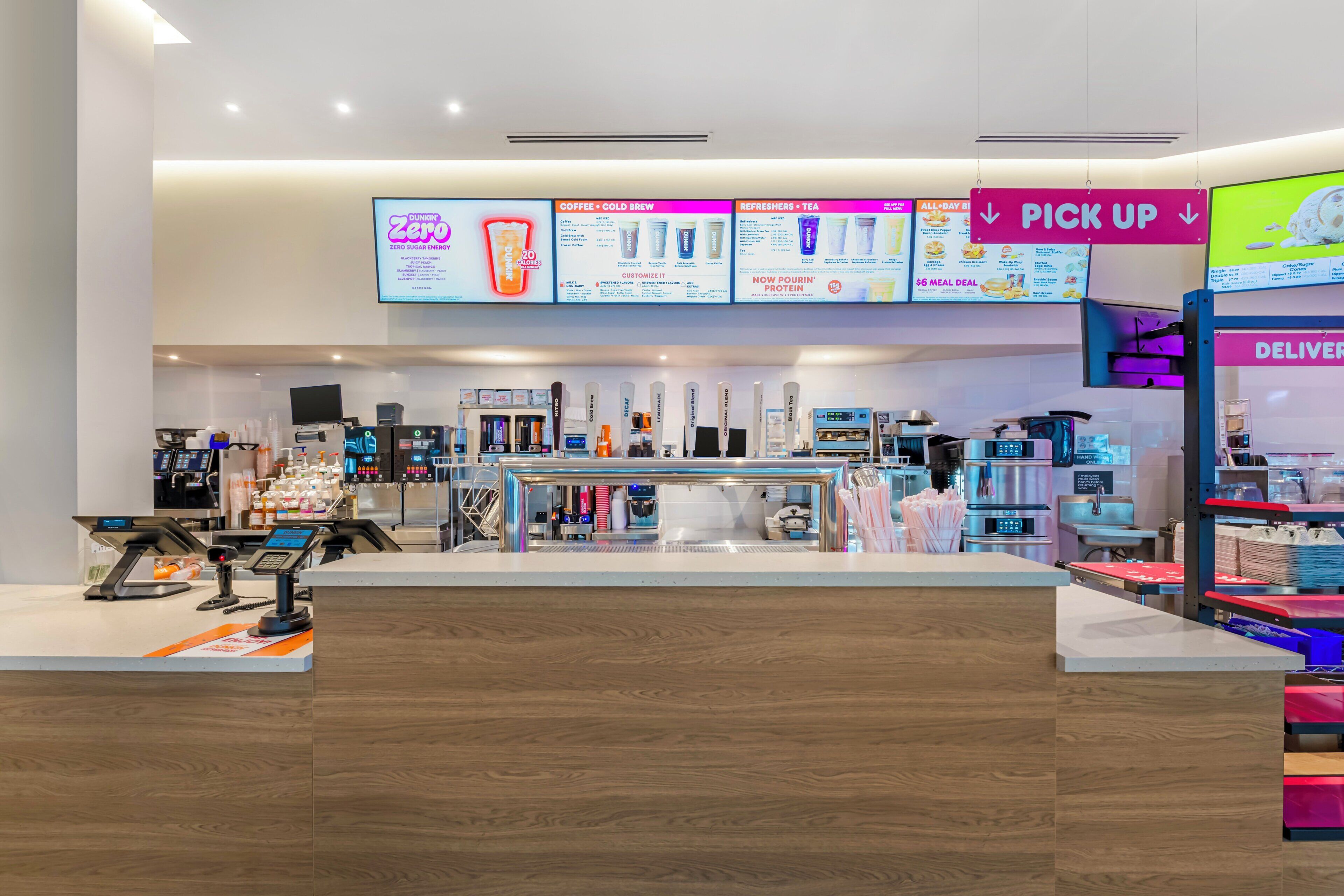 A modern cafe with a pick-up counter, digital menu displays, and a delivery area.