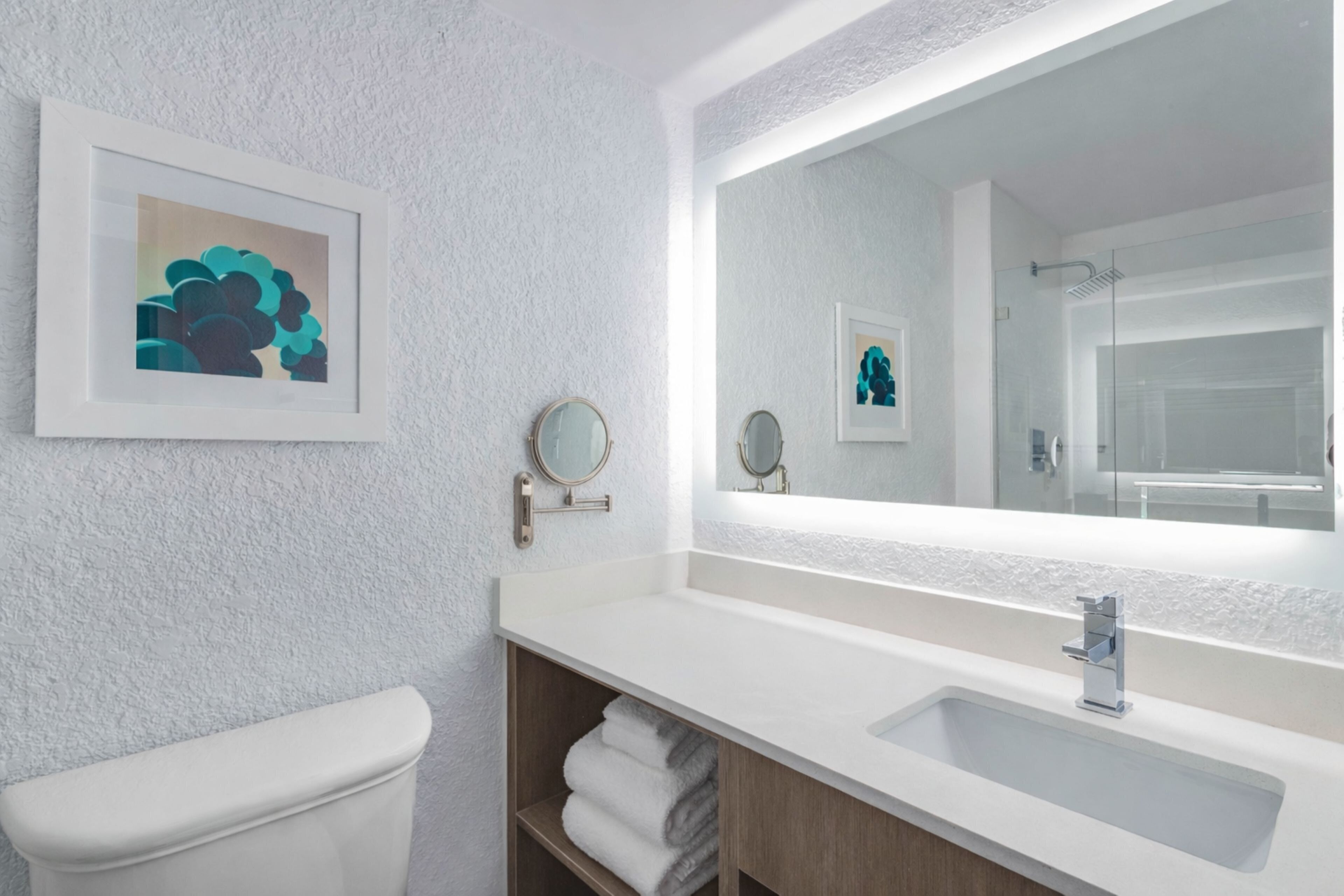 A bathroom with a white toilet, a sink with a mirror, and a framed artwork on the wall.