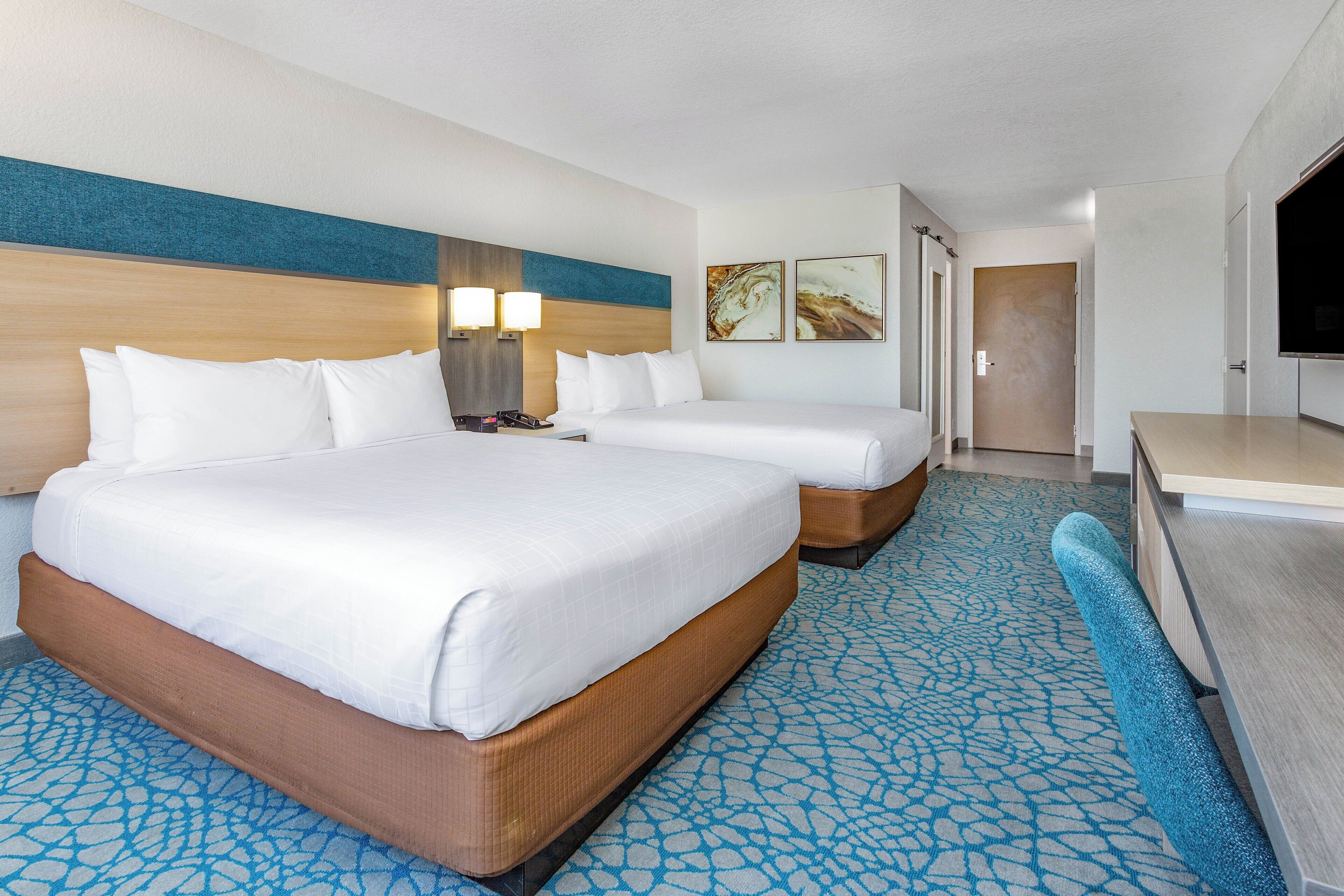 A hotel room with two beds, a desk, a TV, and a bathroom door.