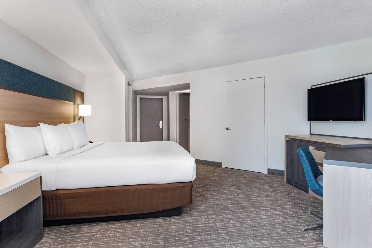 Een hotelkamer met een groot bed, een bureau met stoel, een televisie en een deur naar een andere kamer.