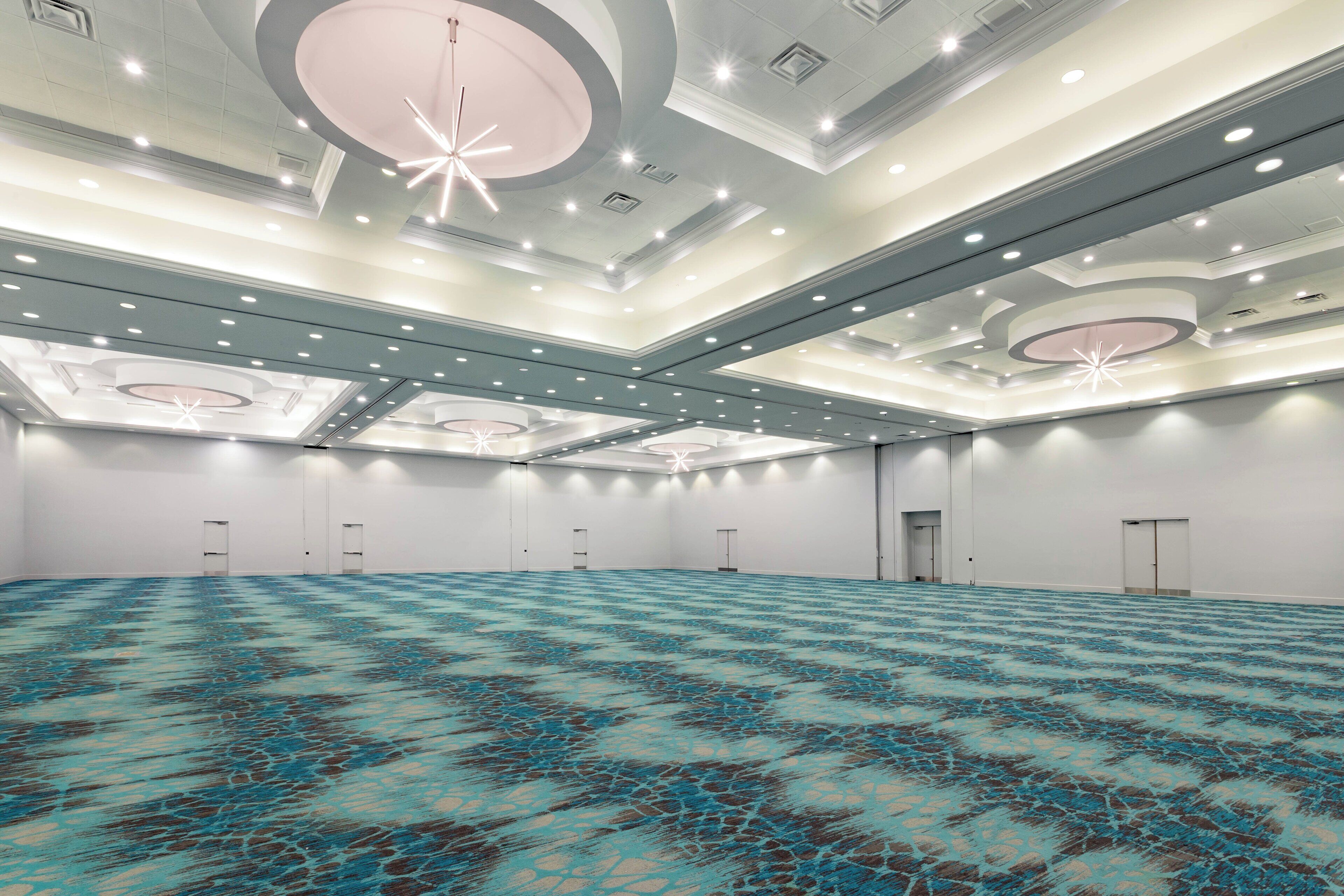 A large, empty conference room with a patterned carpet, recessed lighting, and a modern ceiling design.
