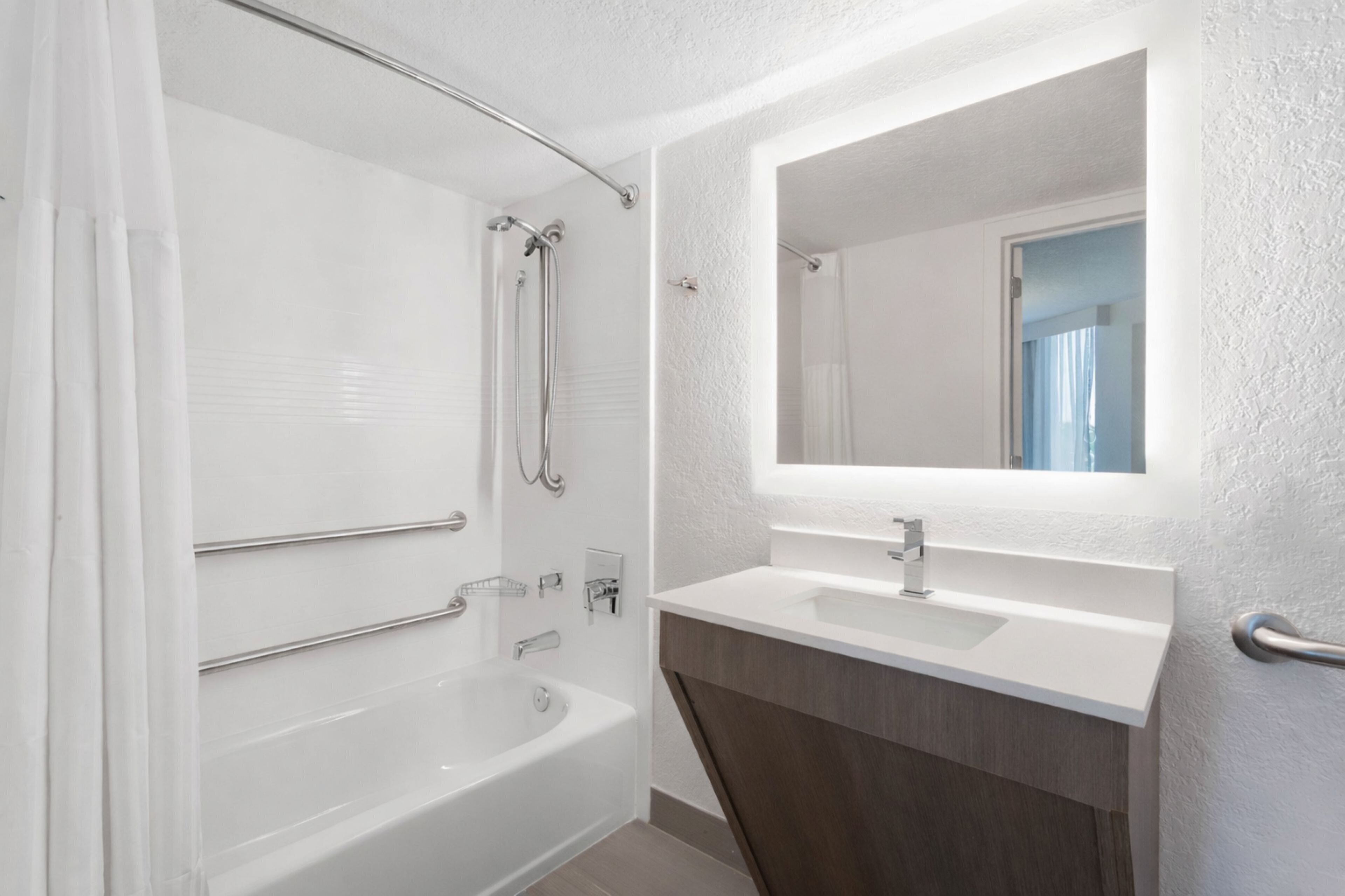 A modern bathroom with a bathtub, a shower, a vanity with a mirror, and a towel rack.
