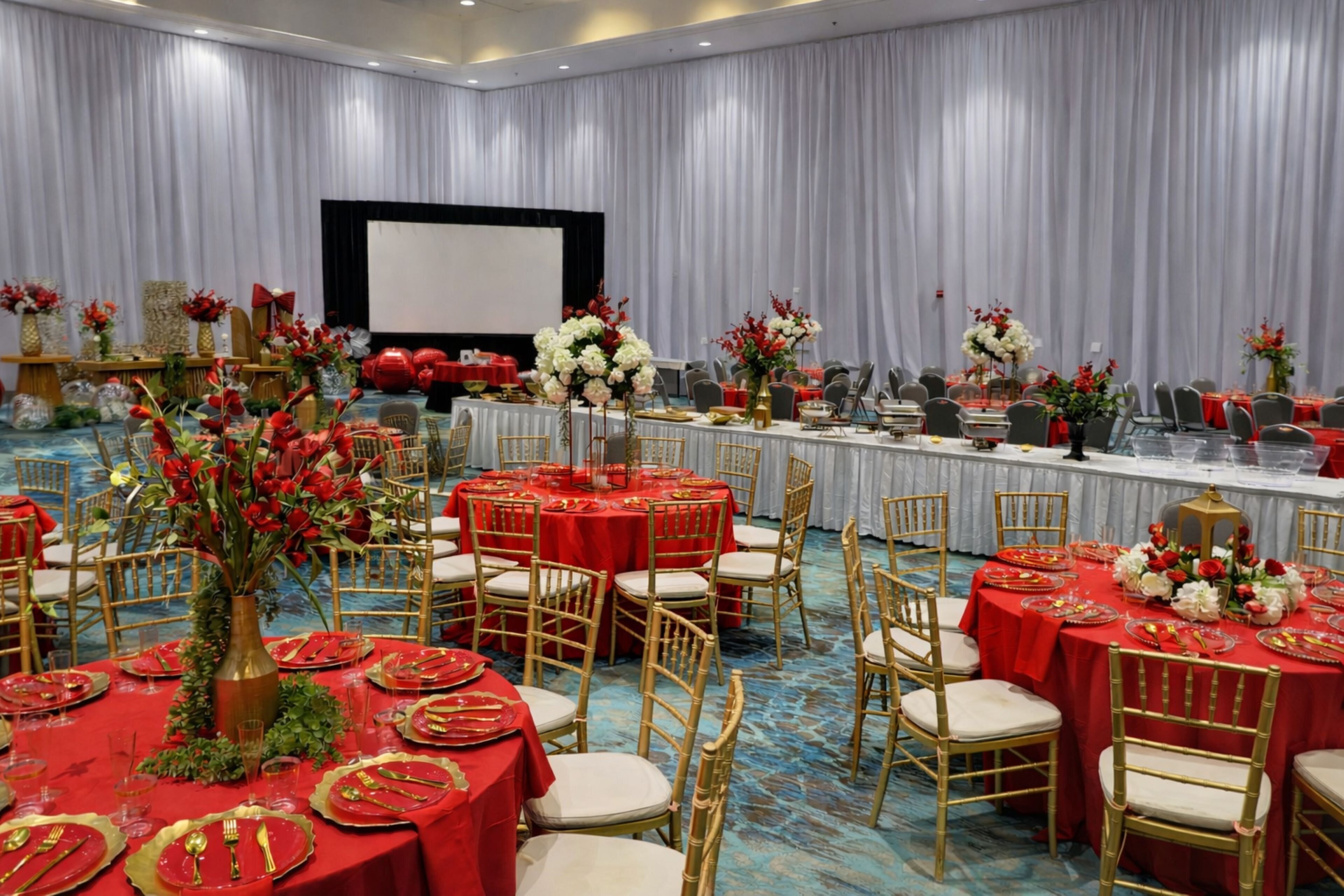 A banquet hall with round tables covered in red tablecloths, gold chairs, and floral centerpieces.