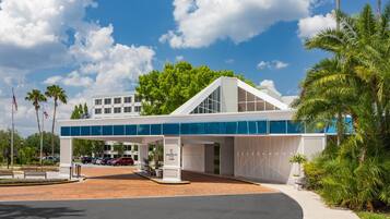 A modern building with a covered entrance, palm trees, and a clear sky.