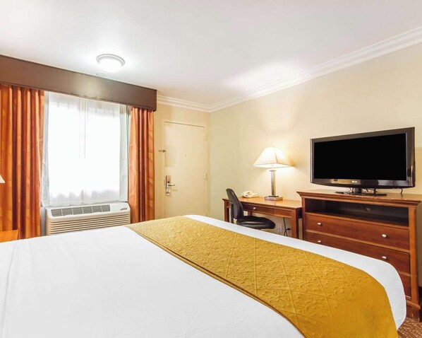 Habitación de hotel con una cama, un escritorio con lámpara, televisión y aire acondicionado.