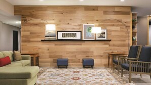 A living room with a wooden wall, two blue ottomans, a green sofa, a patterned rug, and a wooden chair.