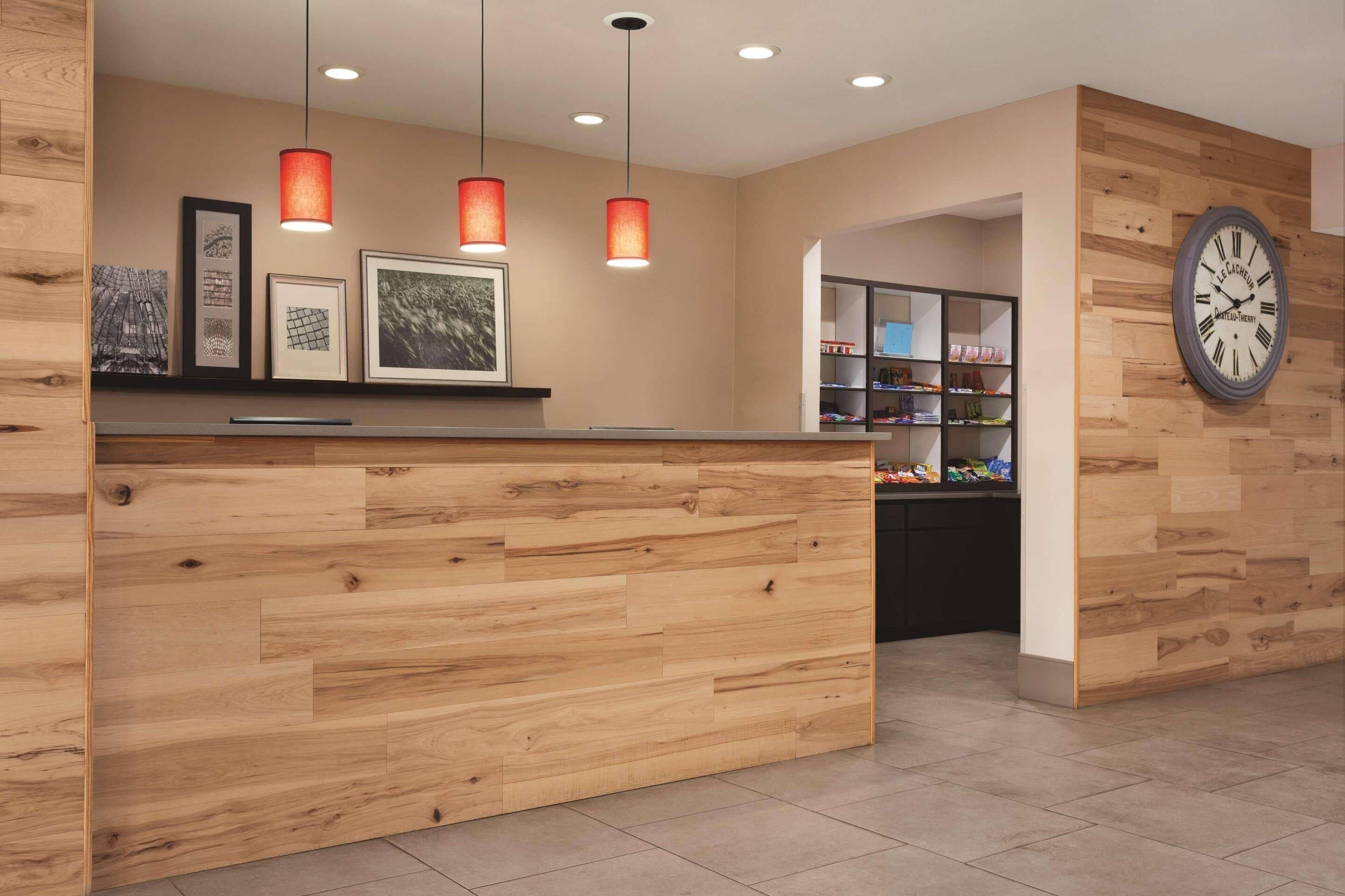 A reception desk with wooden paneling, pendant lights, framed artwork, and a wall clock.