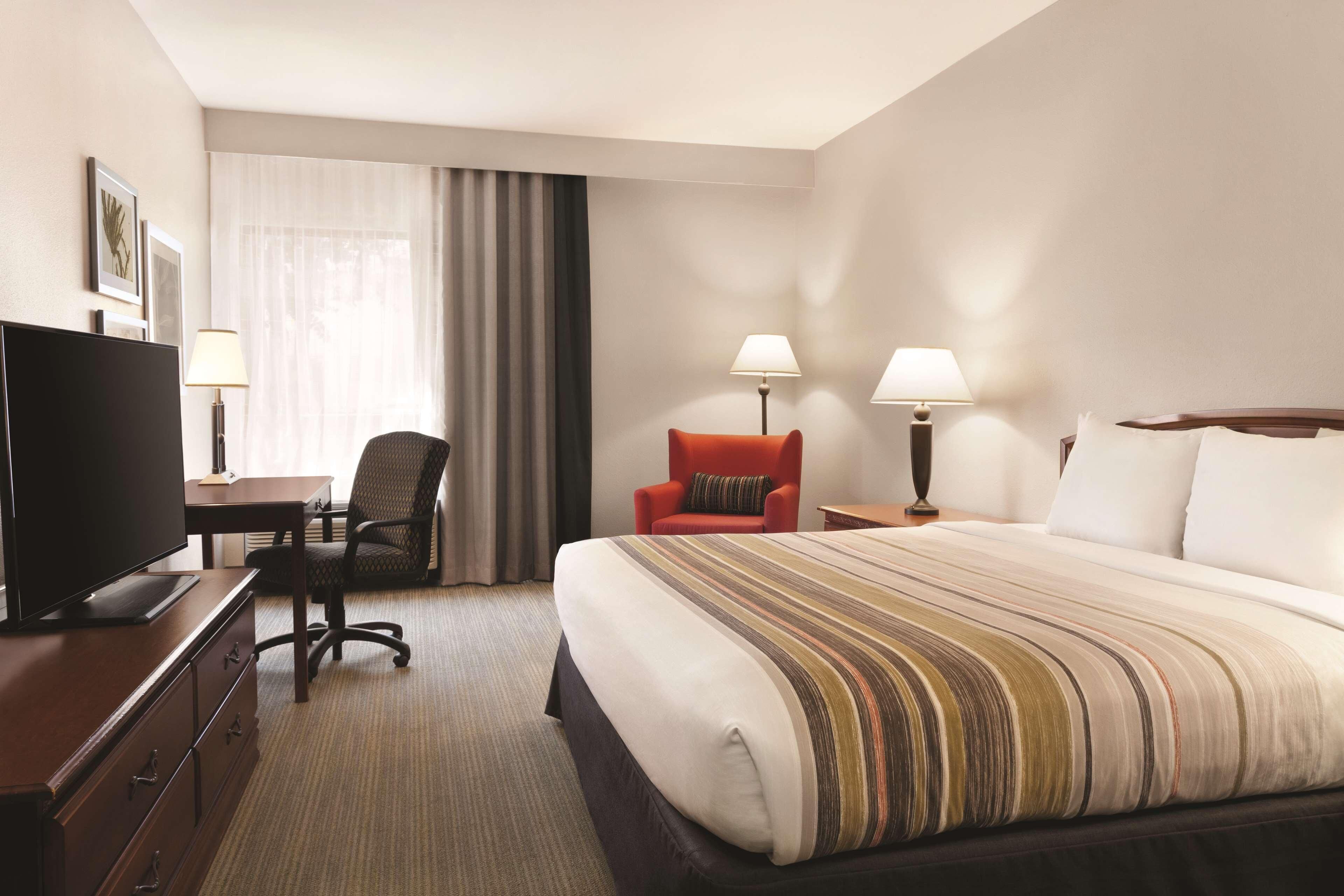 A hotel room with a large bed, a desk with a television, two chairs, and two bedside lamps.