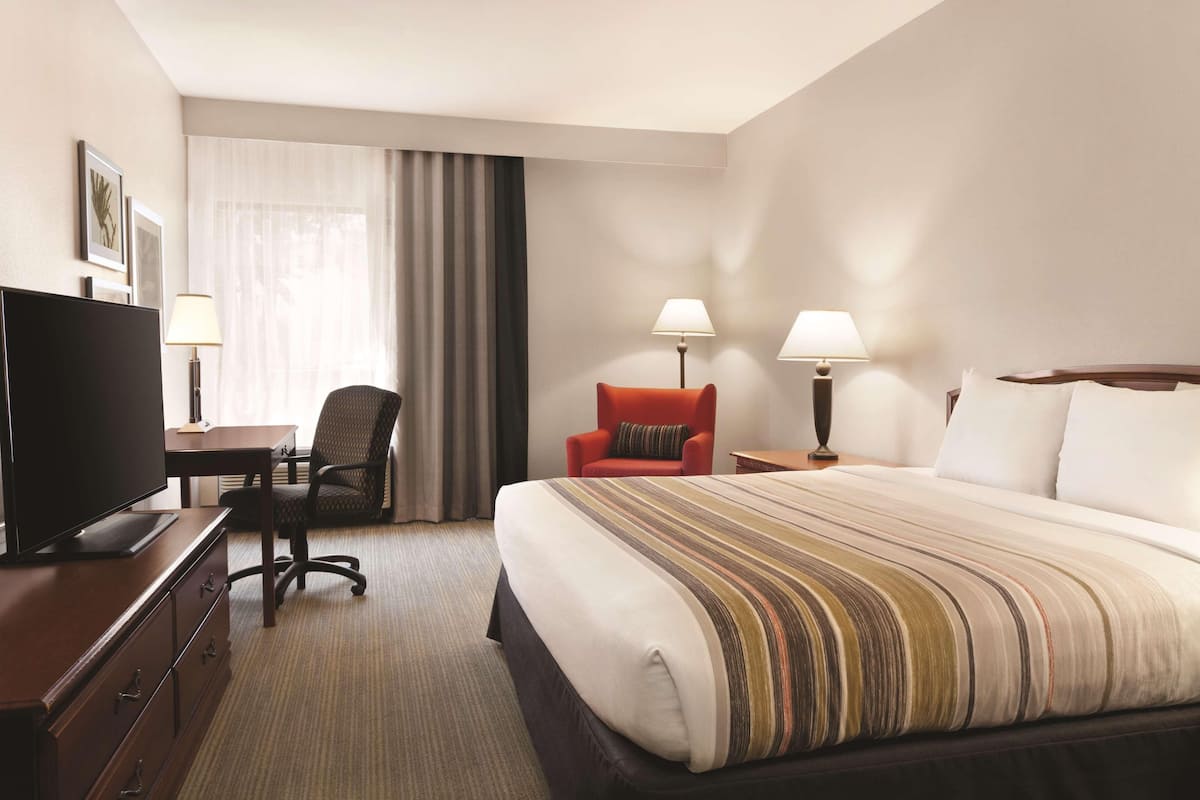 Une chambre d’hôtel avec un grand lit, un bureau avec une télévision, deux chaises et deux lampes de chevet.