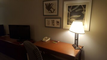 Una habitación de hotel con escritorio, lámpara, teléfono y cuadros en la pared.
