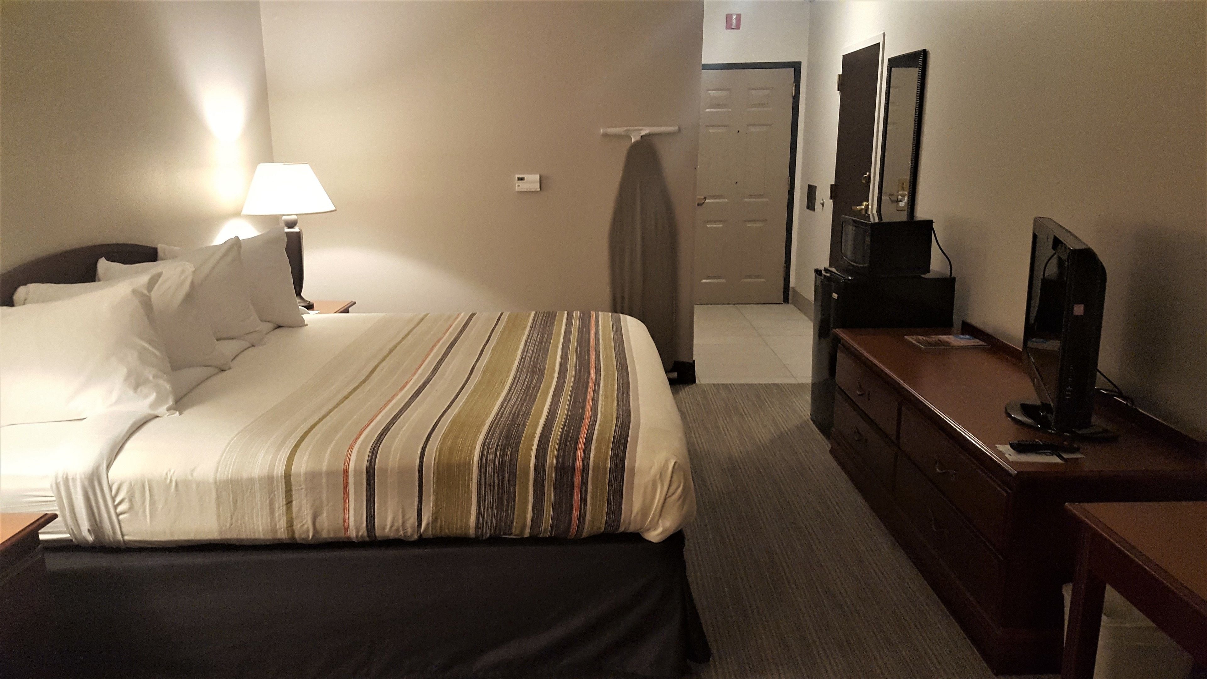 Una habitación de hotel con una cama, un escritorio con una computadora, un televisor y una puerta.